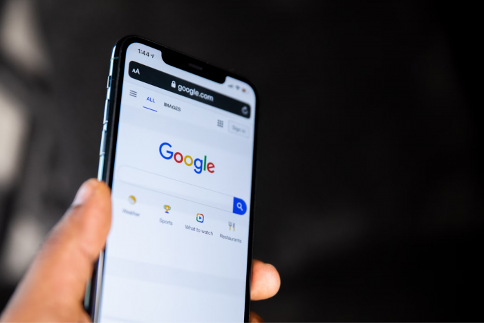 Person holding a smartphone displaying the Google search homepage on the screen.